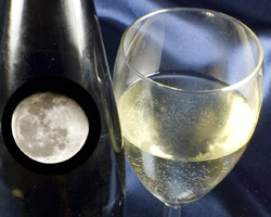 A glass of white wine with the moon reflecting in a wine bottle